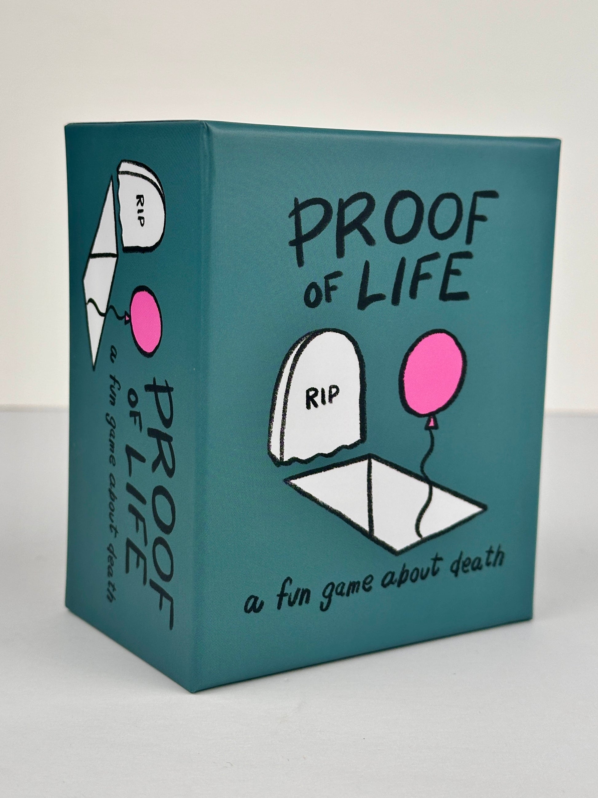 Proof of Life front of box, teal with black writing, an illustrated grave, and a pink balloon
