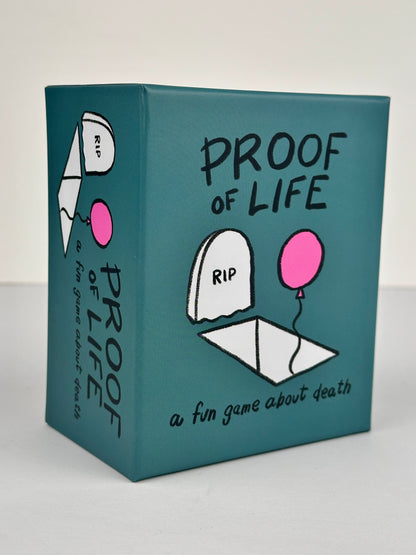 Proof of Life front of box, teal with black writing, an illustrated grave, and a pink balloon